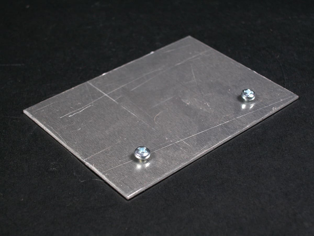 Here's an alt tag for the image: Metal plate with two screws.